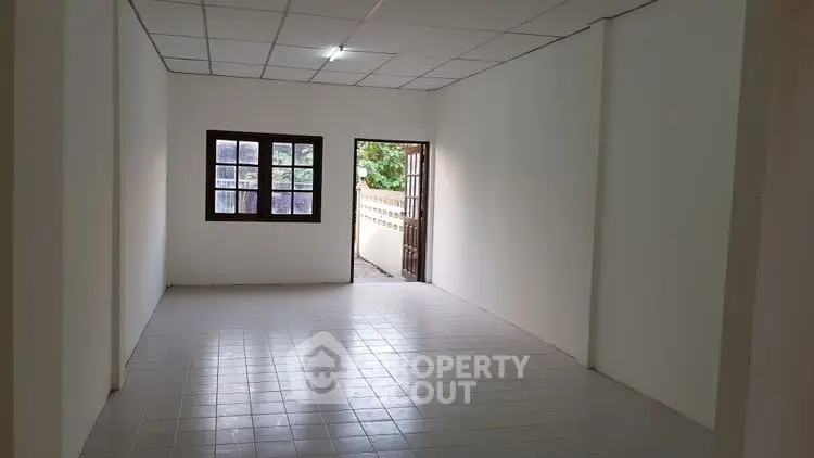 Spacious empty room with tiled floor and natural light from window and door.