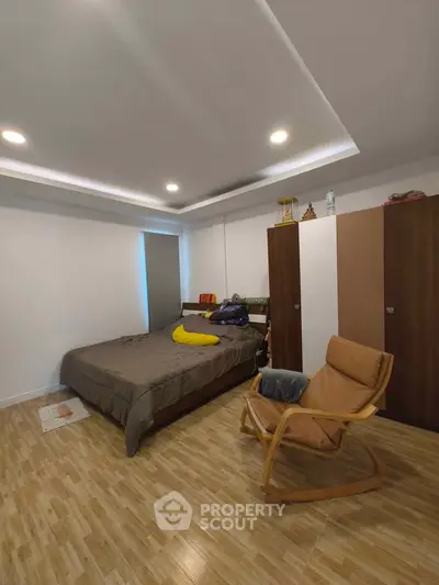 Cozy bedroom with modern lighting and wooden flooring, featuring a comfortable bed and stylish chair.