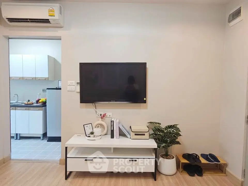 Modern living room with wall-mounted TV and stylish decor, adjacent to a compact kitchen area.