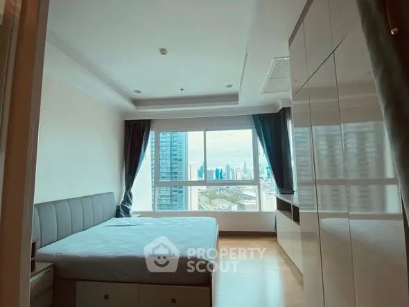 Spacious bedroom with city view and modern furnishings in high-rise apartment.