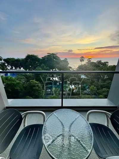 Stunning balcony view with sunset over lush greenery and ocean horizon, perfect for relaxation.