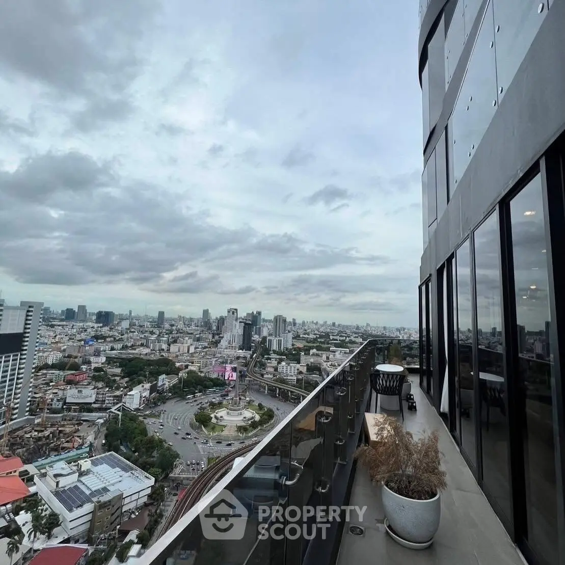 Stunning cityscape view from a high-rise balcony with modern glass railing and outdoor seating.