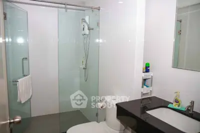 Modern bathroom with glass shower enclosure and sleek black countertop.