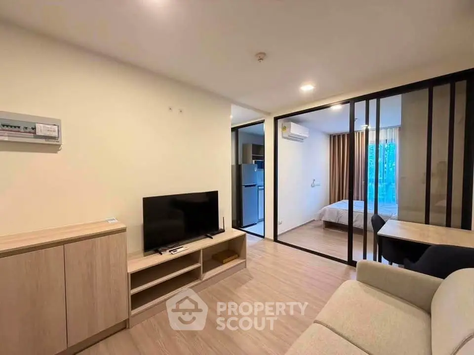 Modern living room with open layout leading to a cozy bedroom, featuring sleek furniture and natural lighting.