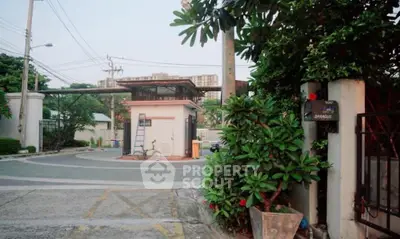 Charming gated community entrance with lush greenery and security post.