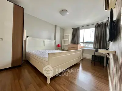 Spacious bedroom with modern furnishings and large window in urban apartment.