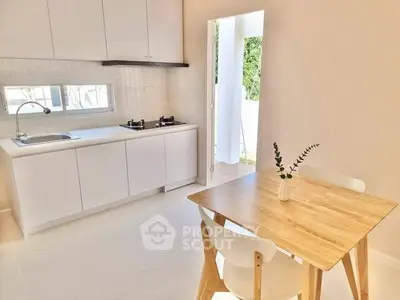 Bright modern kitchen with open layout and dining area, featuring sleek white cabinets and natural light.