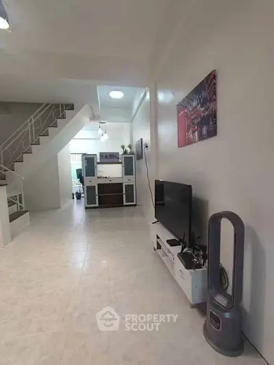Spacious living room with modern decor and open layout, featuring a TV and stylish fan.