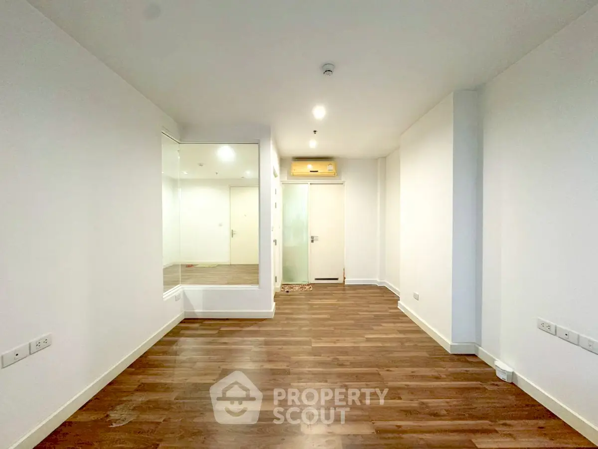 Spacious empty room with wooden flooring and white walls, ideal for customization.