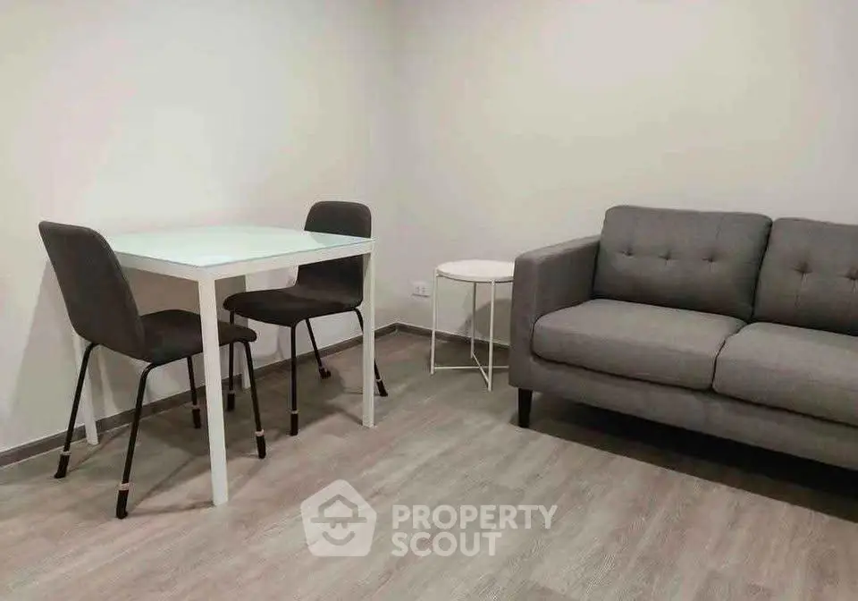 Modern living room with sleek gray sofa and minimalist dining set on wooden flooring.