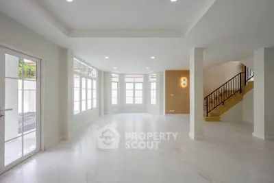 Spacious modern living room with large windows and elegant staircase, perfect for family gatherings.