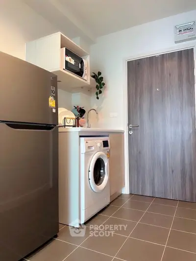 Modern kitchen with stainless steel fridge, washing machine, and microwave in compact layout.