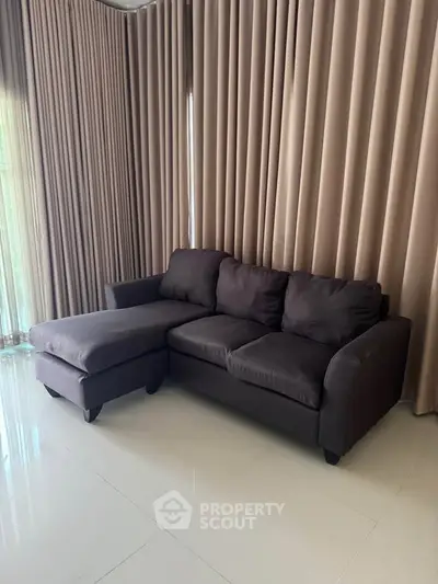 Modern living room with sleek dark sofa and elegant floor-to-ceiling curtains.