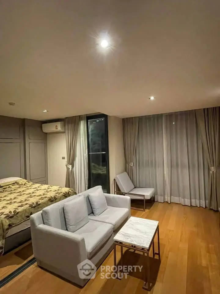 Spacious modern bedroom with cozy seating area and elegant wooden flooring.