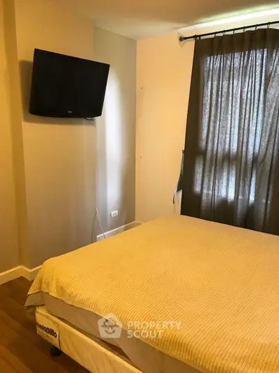 Cozy bedroom with wall-mounted TV and natural light through curtains.