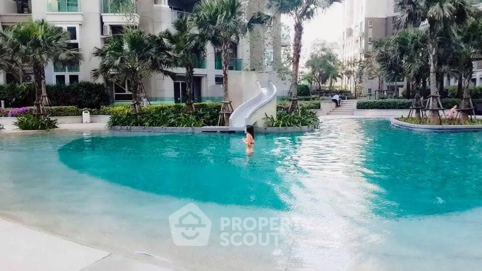 Luxurious residential pool with slide and lush greenery in modern apartment complex.