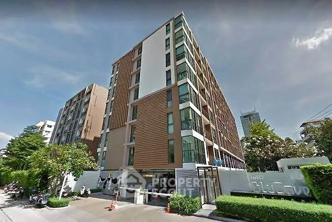 Modern multi-story residential building with lush greenery and clear blue sky.