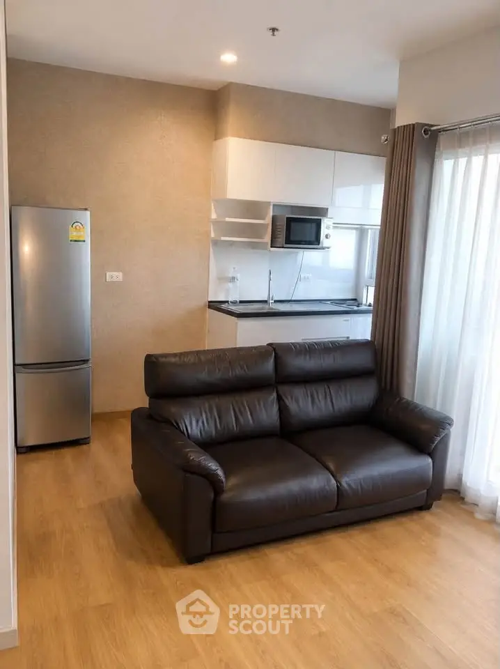 Modern living room with leather sofa and sleek kitchen in open layout apartment.