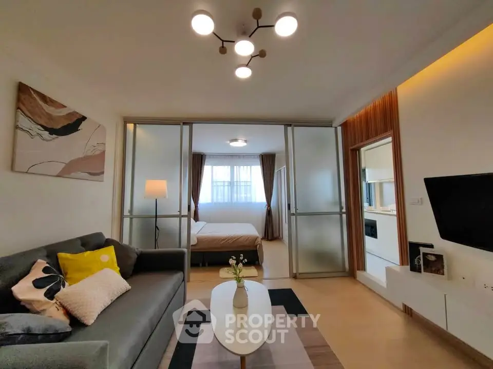 Modern living room with stylish decor and open view to bedroom, featuring cozy seating and elegant lighting.