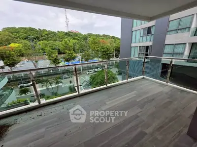 Spacious balcony with modern glass railing and scenic view of lush greenery.
