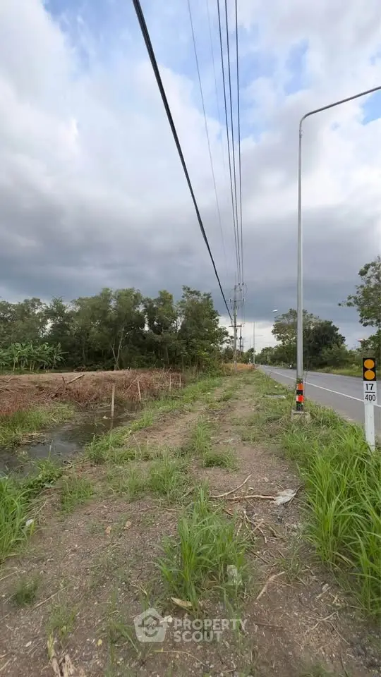 Scenic roadside land plot with lush greenery and clear sky, ideal for development.