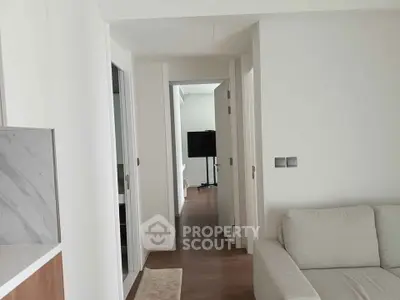 Modern apartment interior with white walls and hardwood floors, featuring a cozy living area and hallway view.