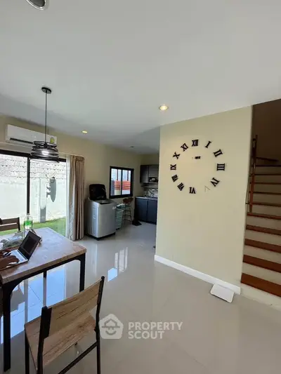 Modern open-plan living area with stylish wall clock and staircase, featuring sleek furniture and natural light.