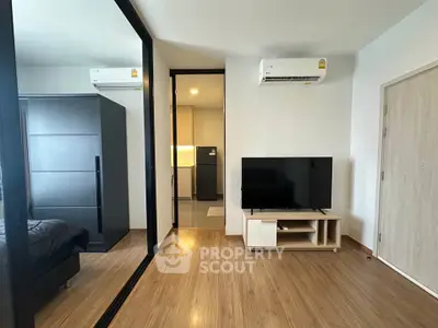 Modern apartment interior with sleek wooden flooring and mirrored wardrobe, featuring a cozy living area with TV.