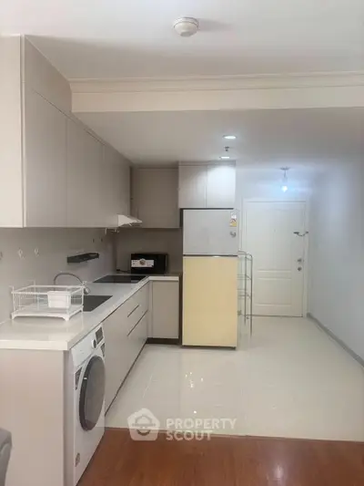 Modern kitchen with sleek cabinetry, washing machine, and fridge in a bright apartment.