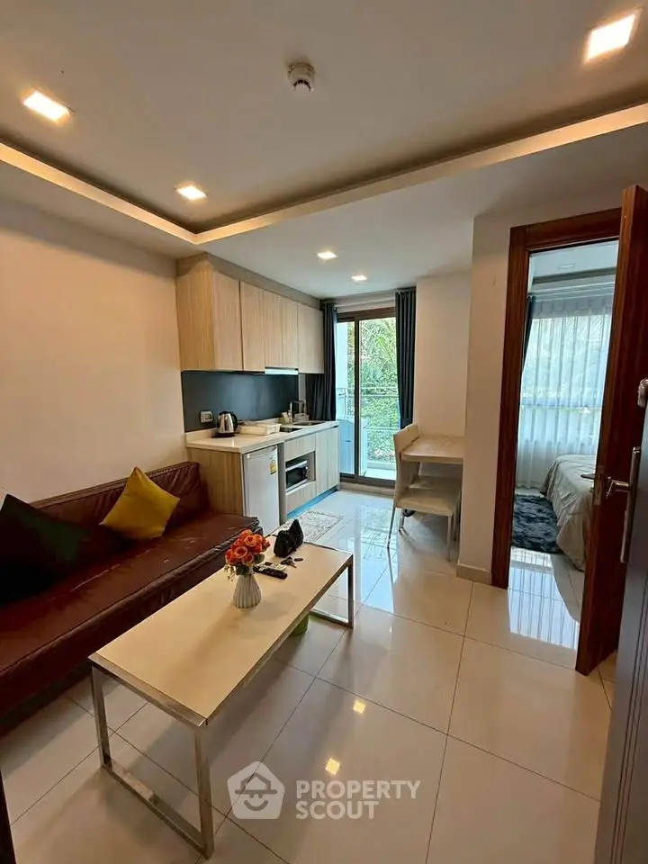 Modern living room with open kitchen and balcony view, featuring sleek furniture and natural light.