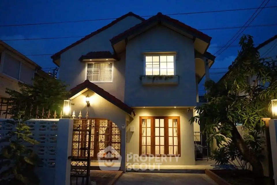 Charming two-story house with warm exterior lighting and lush greenery at dusk.