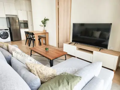 Modern living room with sleek furniture and open kitchen layout, featuring a cozy sofa and large TV.