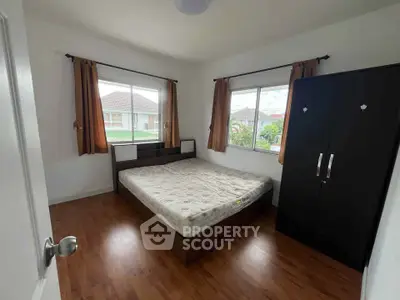 Cozy bedroom with wooden floor and large windows in a serene neighborhood.