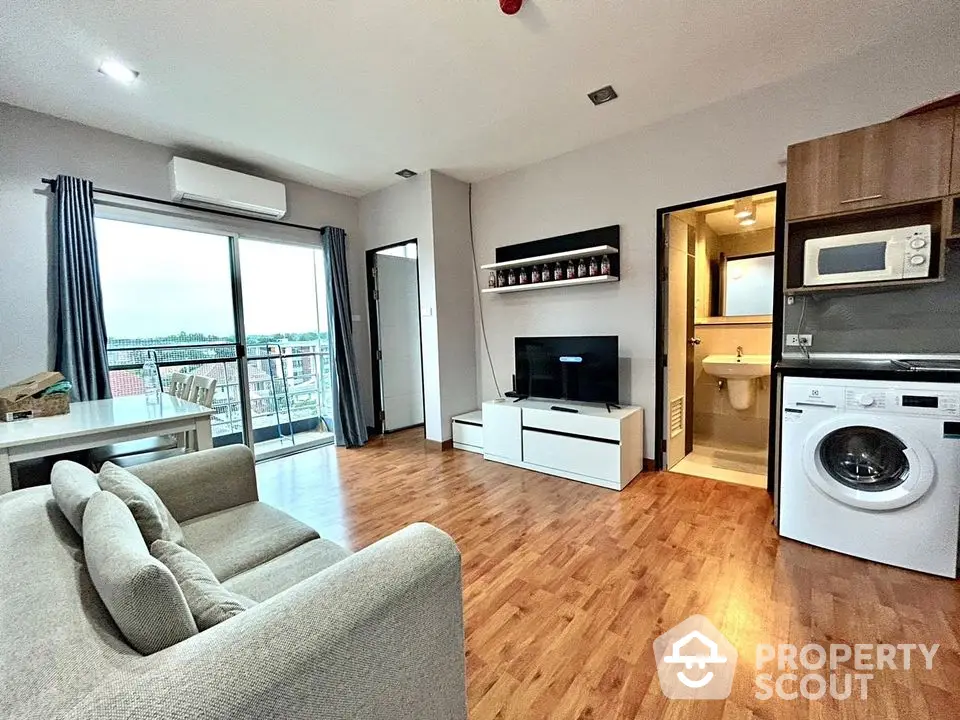 Modern living room with open layout, featuring a washing machine and microwave, overlooking a balcony view.