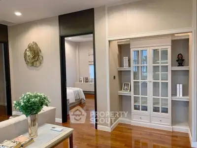Elegant living room with wooden flooring and built-in shelving, leading to a cozy bedroom.