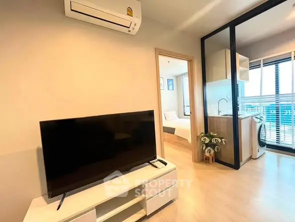 Modern living room with TV and air conditioning, open to a compact kitchen and bedroom.