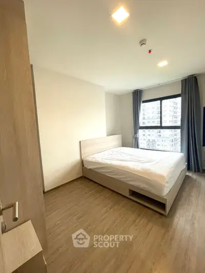Spacious modern bedroom with large window and wooden flooring in urban apartment.