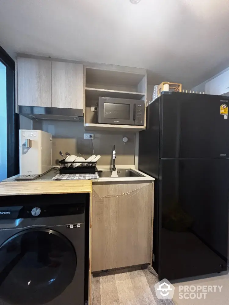 Compact modern kitchen with black fridge, microwave, and washing machine