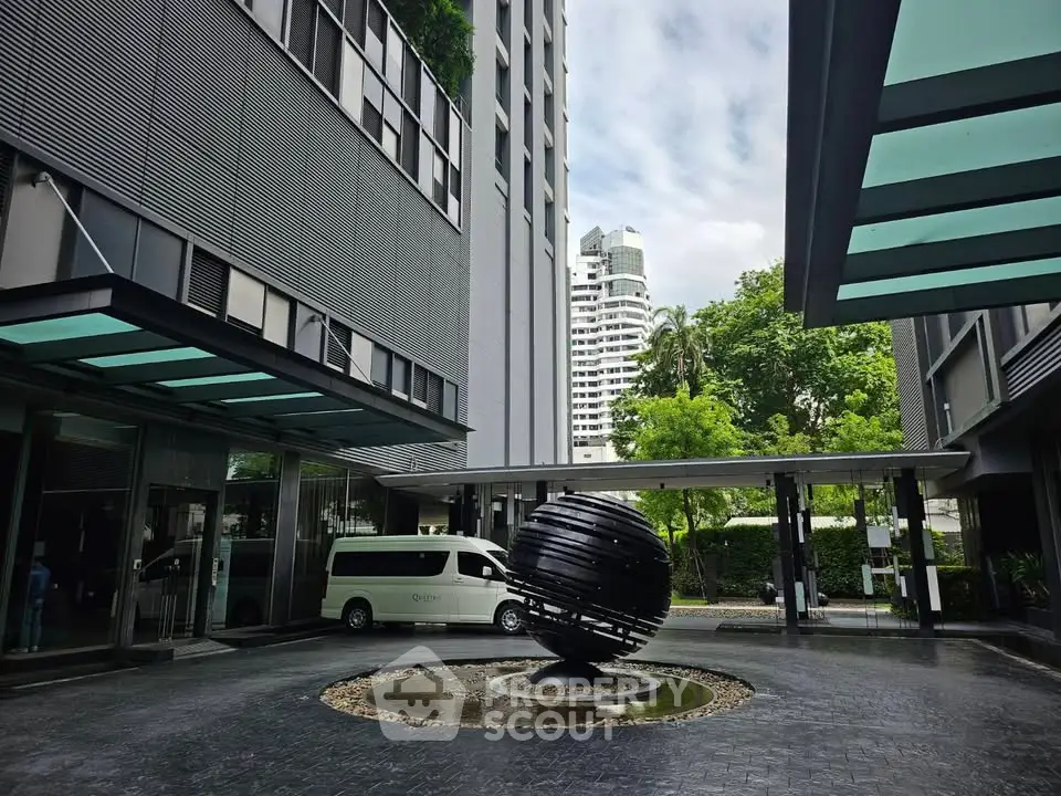 Modern building entrance with unique sculpture and lush greenery