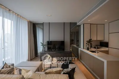 Modern living room with open kitchen, stylish decor, and large windows offering natural light.