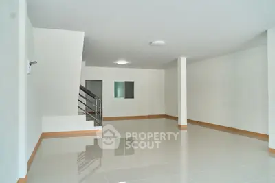 Spacious empty room with glossy tiled floors and staircase, perfect for customization.