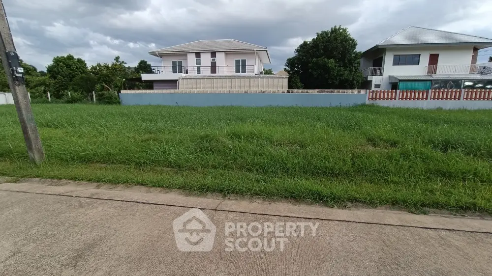 Spacious residential plot with lush greenery and modern houses in serene neighborhood.