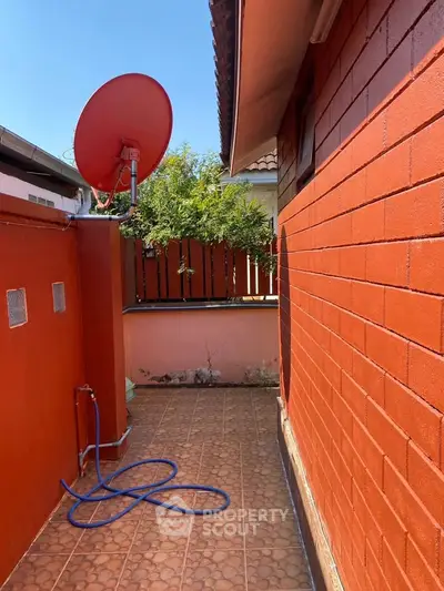 Charming outdoor space with vibrant red brick wall and satellite dish, perfect for urban living.