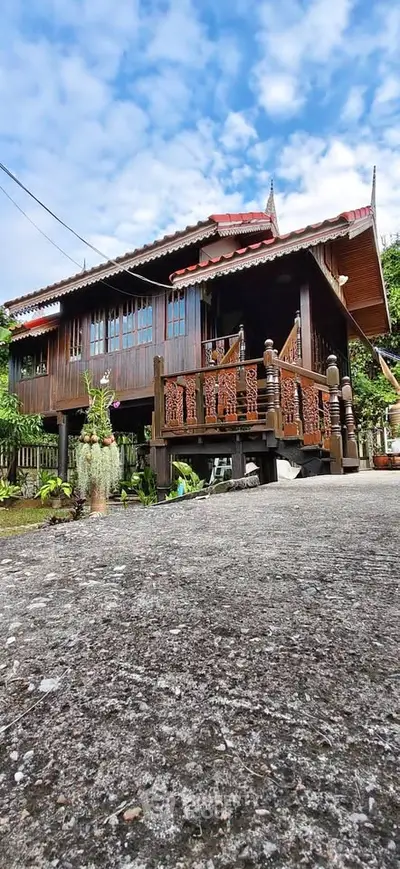 Charming traditional wooden house with intricate detailing and elevated design, surrounded by lush greenery.