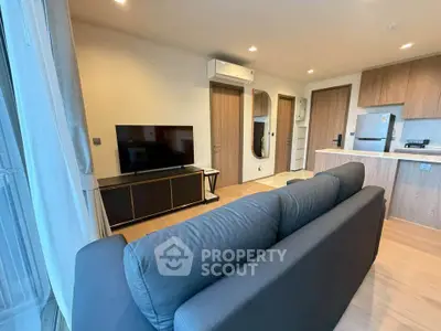 Modern living room with sleek furniture and open kitchen layout, featuring a large TV and stylish decor.