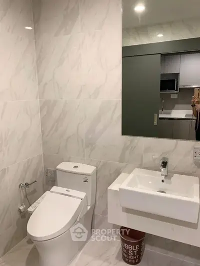 Modern bathroom with sleek fixtures and marble tiles, featuring a stylish toilet and sink.