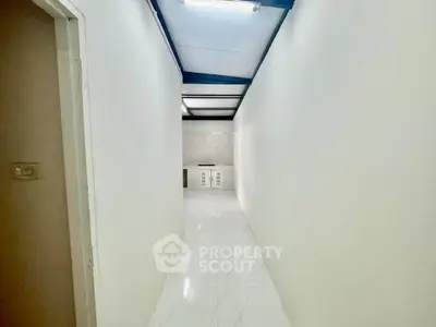 Bright hallway with white walls and glossy floor tiles leading to a small storage area.