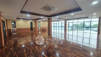Spacious open-plan room with polished wooden floors and large windows offering natural light.