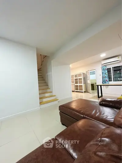 Spacious living room with modern leather sofa and staircase leading to upper floor.