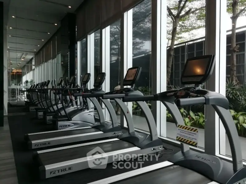Modern gym with multiple treadmills and large windows offering garden views.